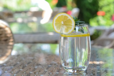 Refreshing water with lemon on glass table in cafe, space for text