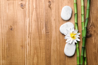 Spa stones, flower and bamboo stems on wooden table, flat lay. Space for text