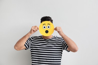 Man hiding emotions using card with drawn surprised face on white background