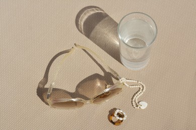 Stylish sunglasses, glass of water and jewelry on grey surface, above view