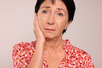 Photo of Senior woman suffering from ear pain on light grey background, closeup