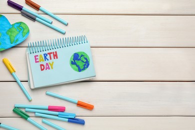 Happy Earth Day. Flat lay composition with notebook and markers on white wooden table, space for text