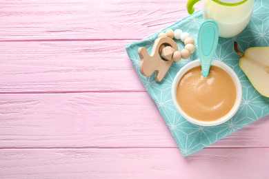 Flat lay composition with bowl of healthy baby food on pink wooden table. Space for text