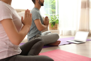 Photo of Couple practicing yoga while watching online class at home during coronavirus pandemic, closeup. Social distancing