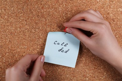 Photo of Woman pinning paper note with phrase Call Dad to cork board, closeup