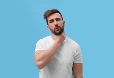 Man suffering from sore throat on light blue background. Cold symptoms