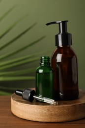 Bottles of hydrophilic oil on wooden table against green background