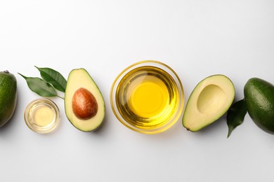 Photo of Cooking oil in bowl and fresh avocados on white background, flat lay