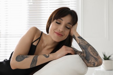 Photo of Beautiful woman with tattoos on arms resting in living room