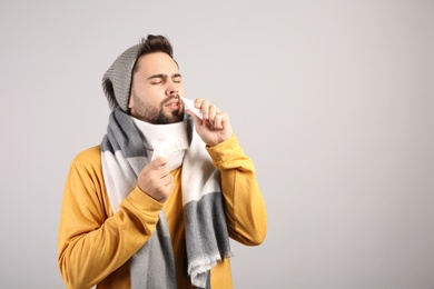Man using nasal spray on light grey background, space for text