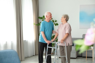 Elderly man and his wife with walking frame indoors. Space for text