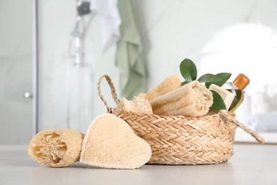 Natural loofah sponges near wicker basket on table in bathroom