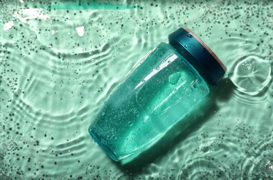 Bottle of hair care cosmetic product in water on turquoise background, top view