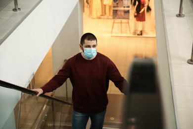 Man with disposable mask on escalator in mall. Dangerous virus