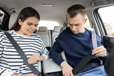 Happy young couple fastening seat belts in car