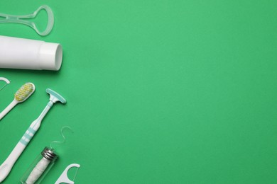 Flat lay composition with tongue cleaners and teeth care products on green background, space for text