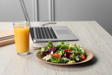 Photo of Fresh vegetable salad, glass of juice and laptop on white wooden table at workplace. Business lunch