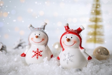 Christmas composition with decorative snowmen on artificial snow against blurred festive lights