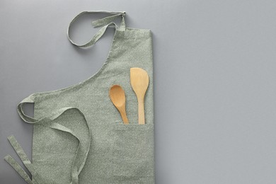 Photo of Clean apron with wooden kitchen tools on light grey background, top view. Space for text