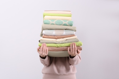 Woman holding stack of clean bed linens on light background