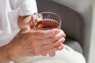 Elderly woman with cup of hot tea indoors, closeup. Home care service