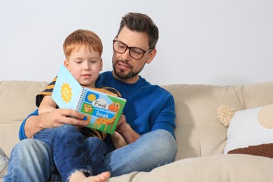 Photo of Father reading book with his son on sofa in living room at home