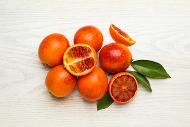 Many ripe sicilian oranges and leaves on white wooden table, flat lay