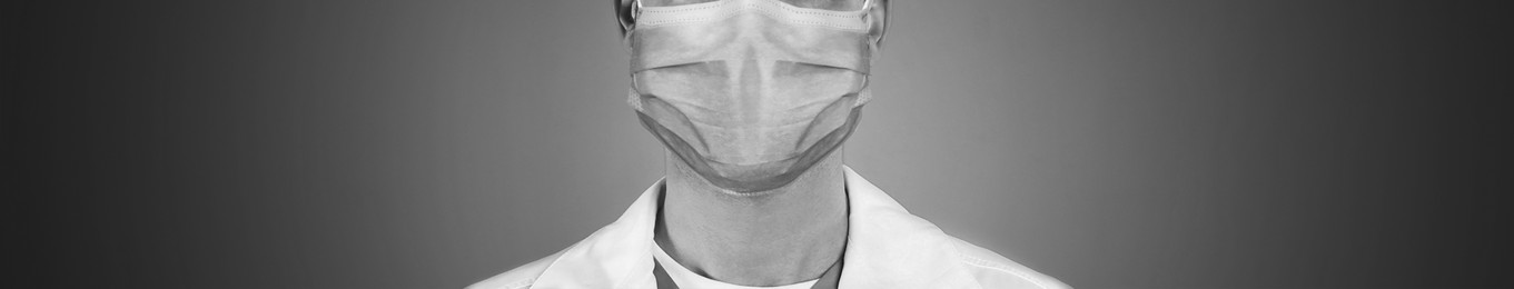 Closeup view of man wearing medical face mask on grey background, banner design. Black and white photography