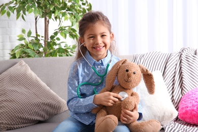 Cute child imagining herself doctor while playing with stethoscope on sofa in living room