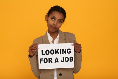 Photo of Unemployed African American woman holding sign with phrase Looking For A Job on orange background