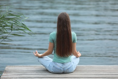 Teenage girl meditating near river, back view