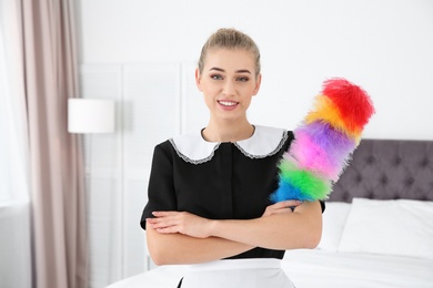 Young chambermaid with dust brush in bedroom