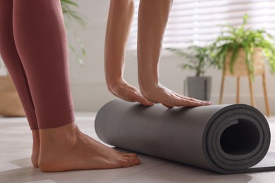 Photo of Woman unrolling yoga mat at home, closeup