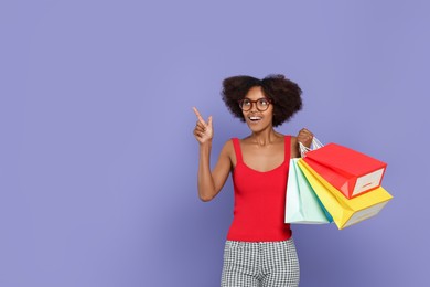Photo of Happy African American woman in glasses with shopping bags on purple background. Space for text