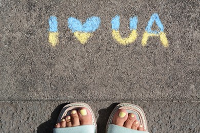 Woman near inscription I love Ukraine drawn by blue and yellow chalk on asphalt, top view