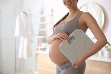 Young pregnant woman with scales in bathroom, closeup