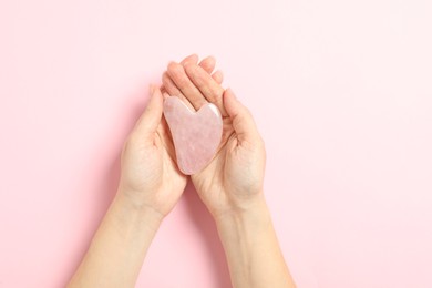 Photo of Woman with rose quartz gua sha tool on light pink background, closeup