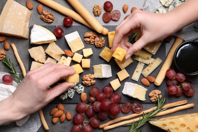 Women taking pieces from cheese plate on dark table, top view