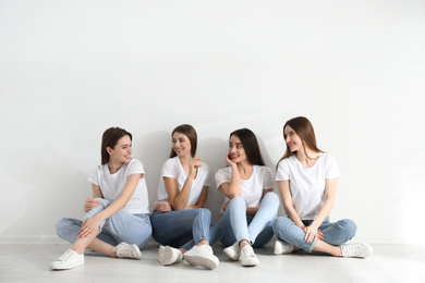 Photo of Beautiful young ladies in jeans and white t-shirts near light wall indoors. Woman's Day