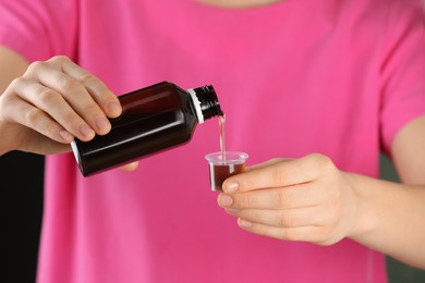 Woman pouring cough syrup into measuring cup, closeup