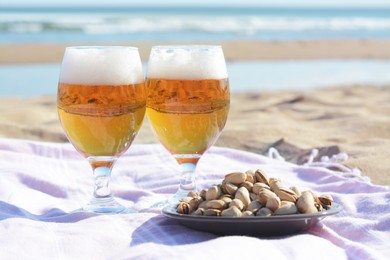 Glasses of cold beer and pistachios on sandy beach near sea
