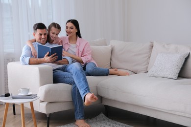 Father reading book to family on sofa in living room
