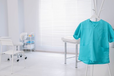Photo of Turquoise medical uniform on rack in clinic. Space for text