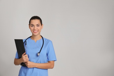 Portrait of young medical assistant with stethoscope and clipboard on color background. Space for text