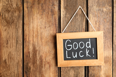 Blackboard with phrase GOOD LUCK hanging on wooden wall. Space for text