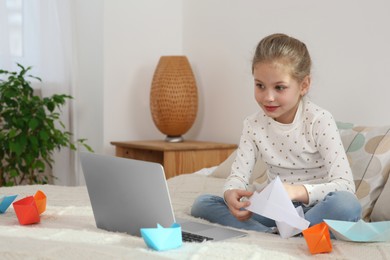 Photo of Little girl learning to make paper boats with online course at home. Space for text