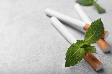 Menthol cigarettes and mint leaves on grey table, closeup. Space for text