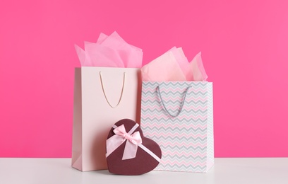 Gift bags and box on white table against pink background