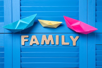 Photo of Paper ships and word Family on blue wooden background, flat lay