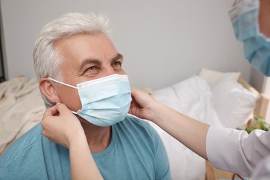 Doctor putting protective mask on senior man at nursing home